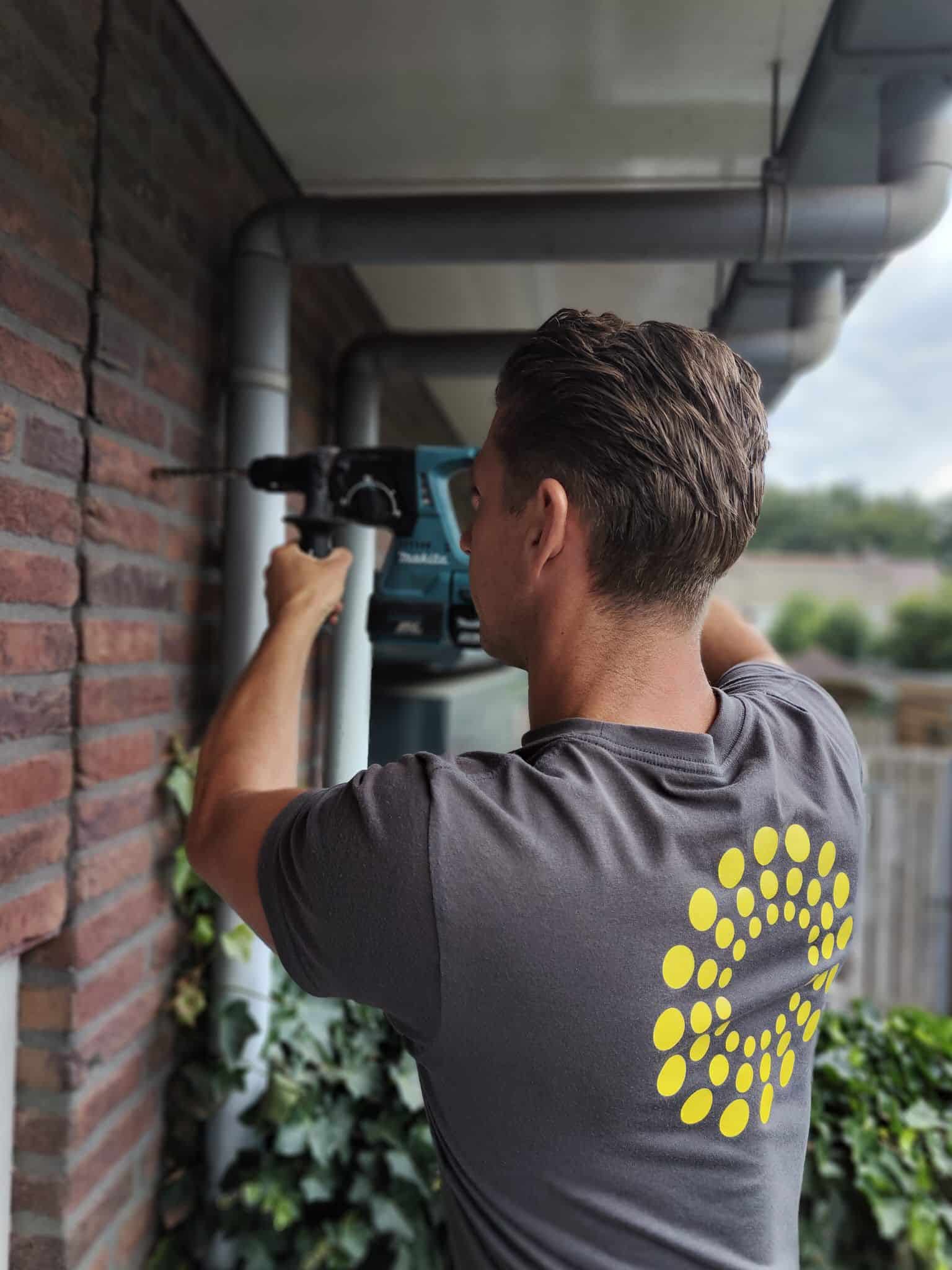 Op de foto staat Paul de Boer die een gat boort om zonwering te monteren