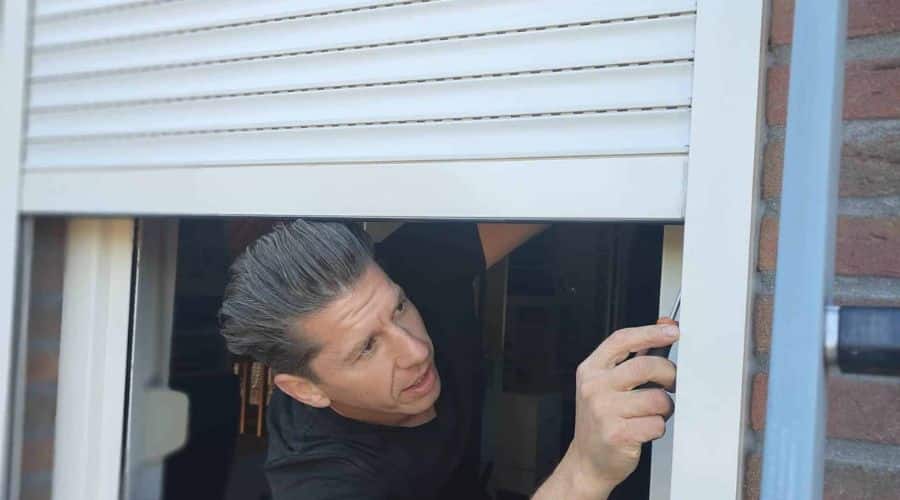 Op de foto is Paul van zonwering de boer te zien, die een reparatie aan een rolluik uitvoert.