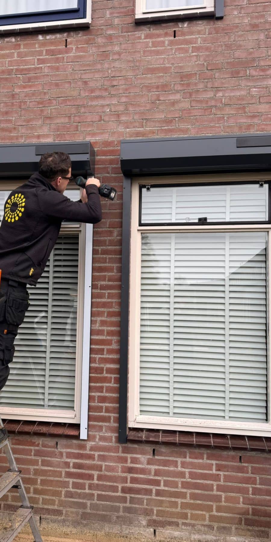 Op deze foto is een monteur van zonwering de boer te zien die een solar rolluik aan het monteren is